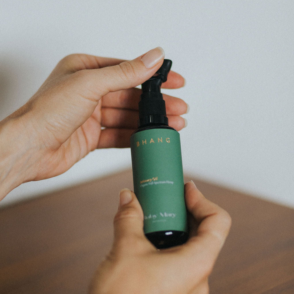 Hand holding a green spray bottle with a white label on a wooden surface.