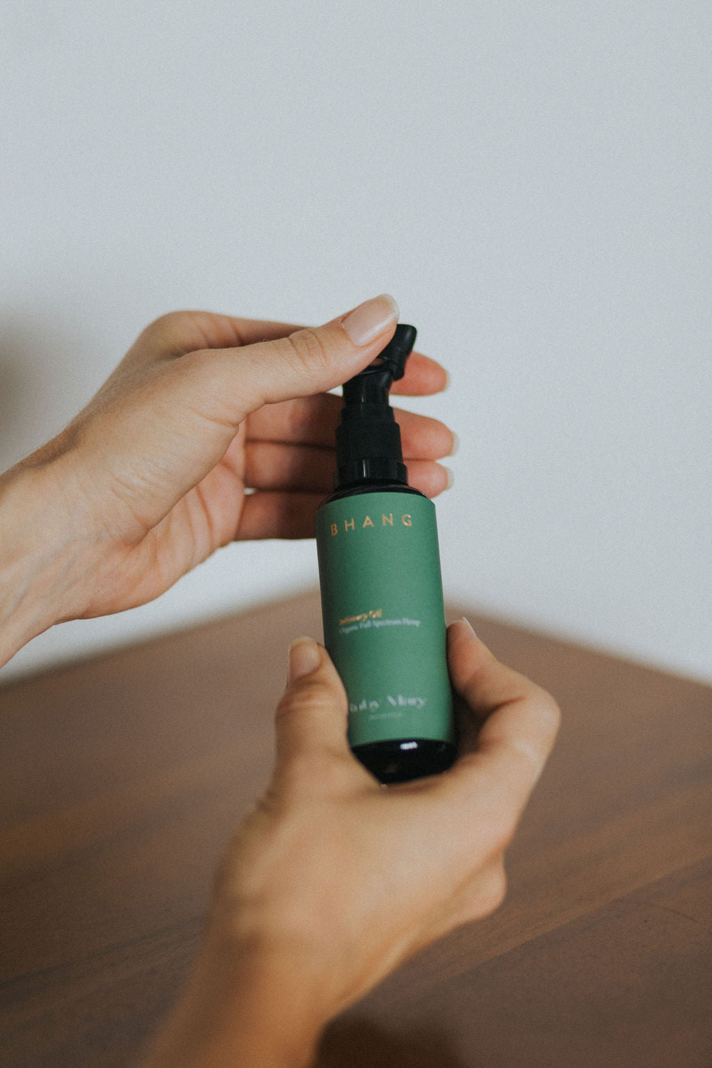 


Hand holding a green spray bottle with a white label on a wooden surface.