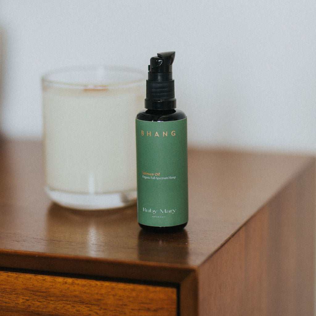 Green bottle with black pump on a wooden surface next to a candle
