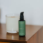 Green bottle with black pump on a wooden surface next to a candle
