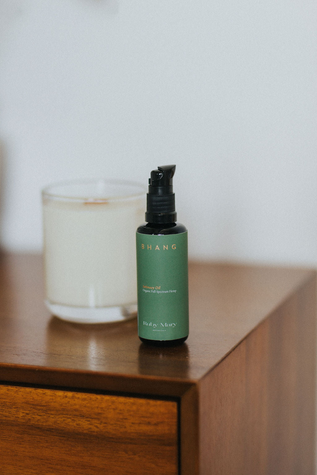 Green bottle with black pump on a wooden surface next to a candle
