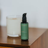 Green bottle with black pump on a wooden surface next to a candle
